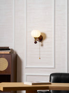 A smaller view of this Clérachic wall light on a panelled wall, with a wooden cabinet, a stack of books and a leather chair.