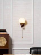 Clérachic wall light centred on a white wall panel, with the cabinet and a dark leather chair at the bottom of the frame.