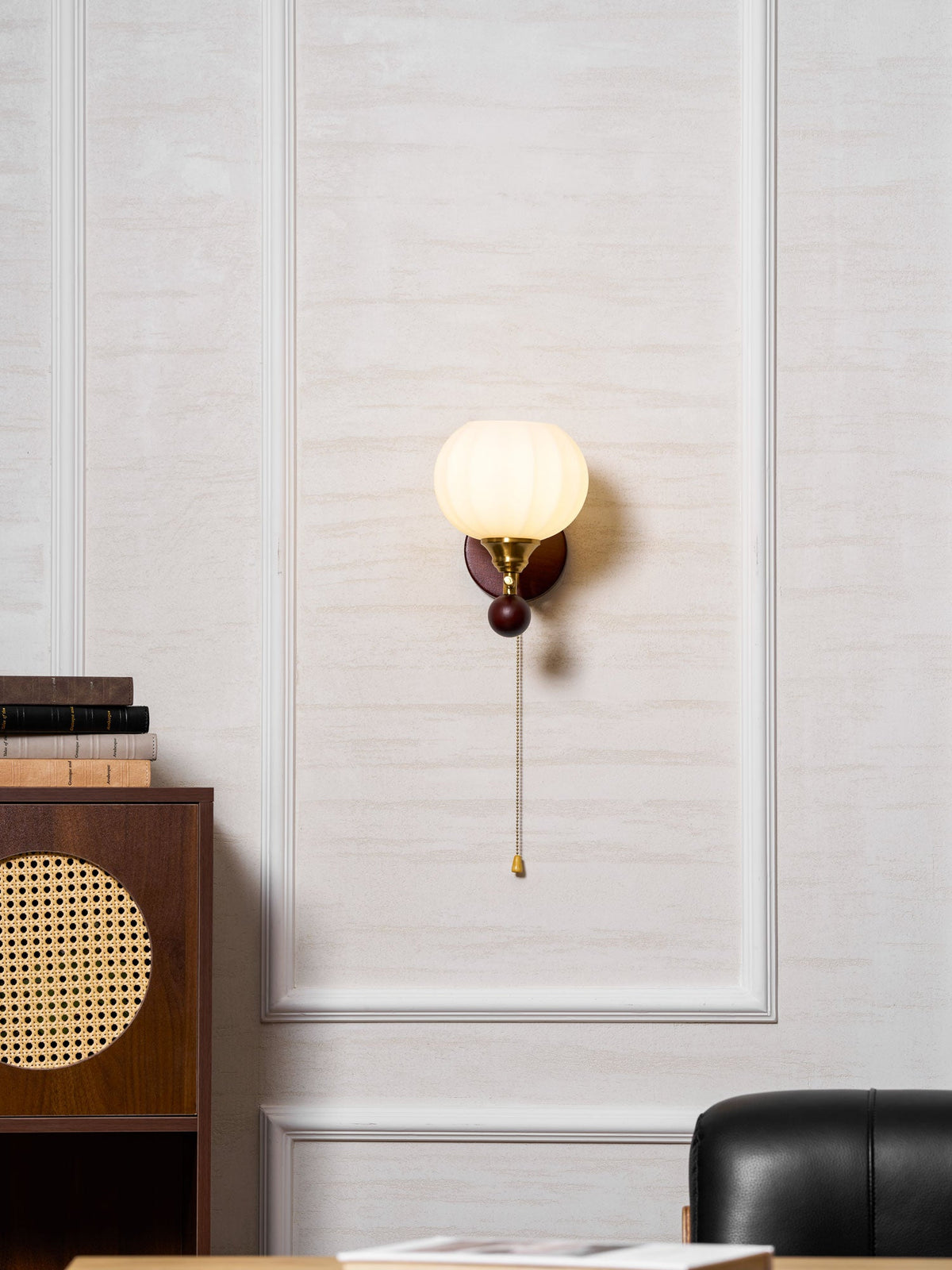 Clérachic wall light centred on a white wall panel, with the cabinet and a dark leather chair at the bottom of the frame.