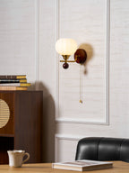 A Clérachic wall light high on a panelled wall, above a rattan-panel cabinet, a teacup, an open book and a leather chair.