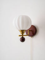 Close view of the ribbed white glass globe, gold arm and walnut-toned ball on this Clérachic wall light, against a plain white wall.