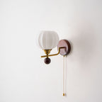 Clérachic wall light on a plain pale wall, with a ribbed frosted globe, gold arm, walnut-toned backplate and pull chain.