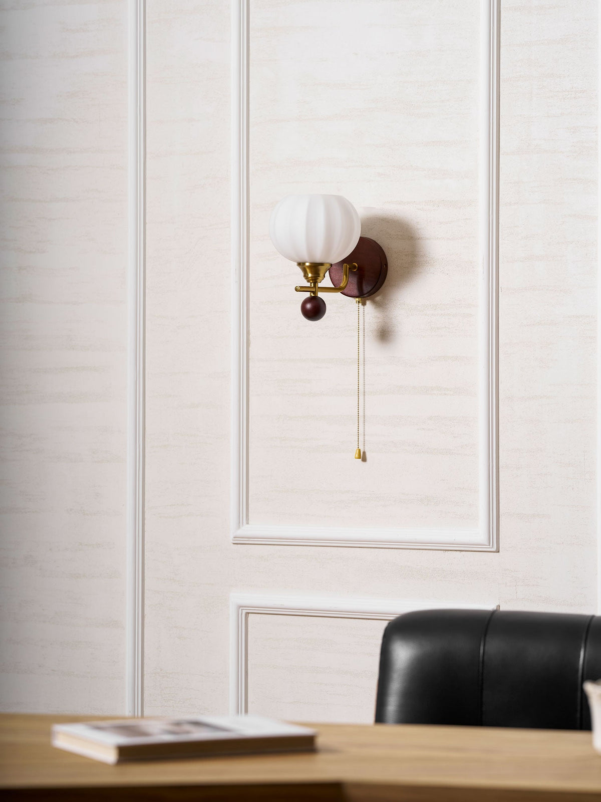 Small in the frame, this Clérachic wall light sits high on a panelled wall above a desk with an open book and a leather chair.