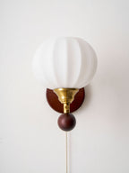 Front view of the ribbed glass globe on this Clérachic wall light, with its gold fitting, walnut-toned ball and pull chain.
