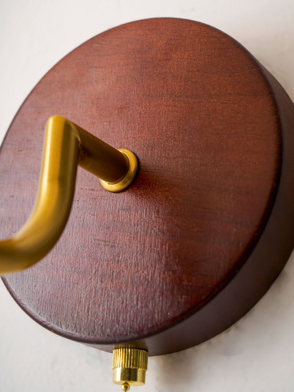 Close view of the round walnut-toned backplate, gold arm joint and brass chain end of this Clérachic wall light.
