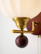 Close view of the gold socket cup, crossbar and dark wooden ball under the ribbed glass globe of this Clérachic wall light.