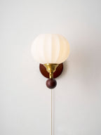 Front view of this Clérachic wall light on a pale grey wall, with its ribbed globe lit softly and the pull chain hanging below.
