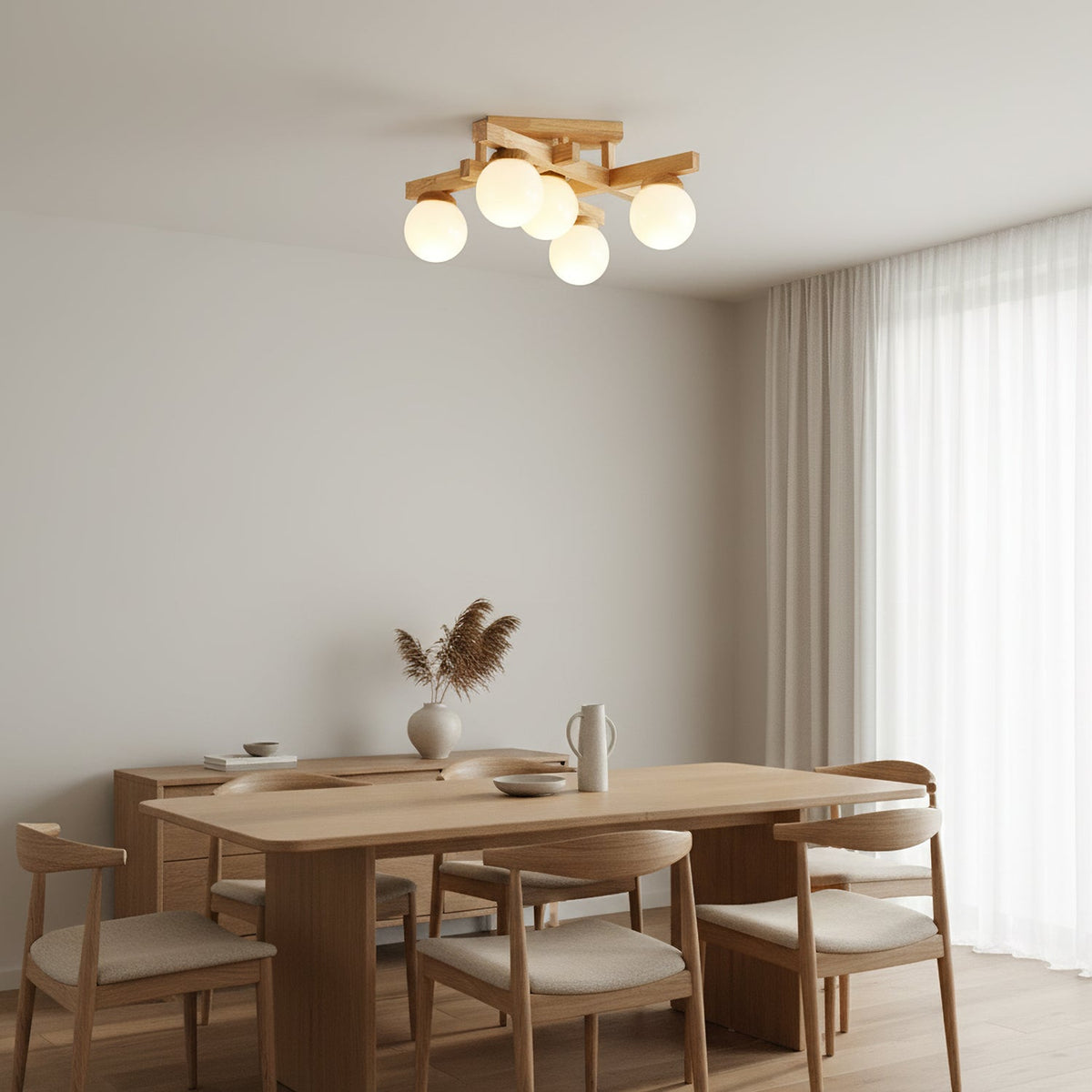 A five-globe Clérachic ceiling light with a wood frame glowing over an oak dining table, with curved-back chairs and dried grasses in a vase.