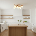 Wood-and-glass Clérachic flush-mount light hanging above a wood-topped kitchen island, with white cabinets and open timber shelves behind.