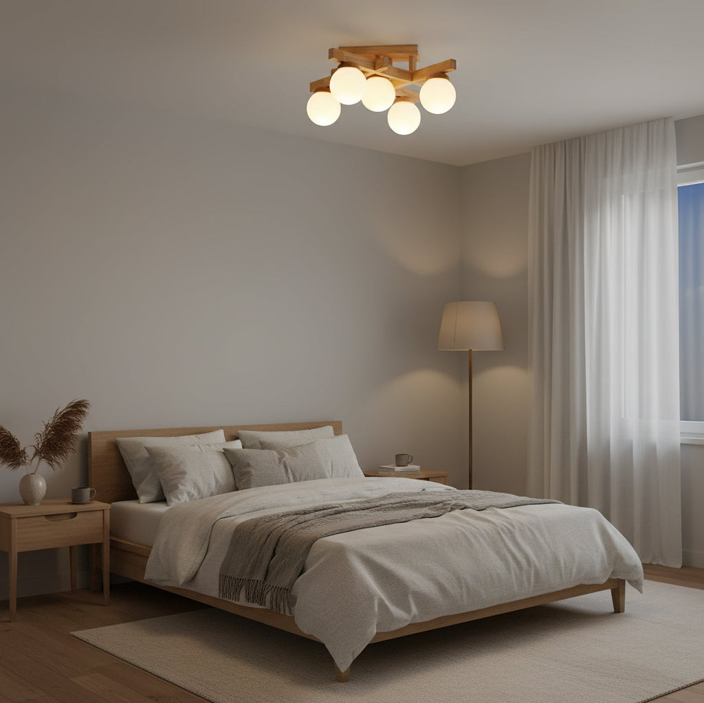 Five frosted globes on a wood frame, this Clérachic ceiling light lit above a bedroom with a grey-covered bed, floor lamp and sheer curtains.