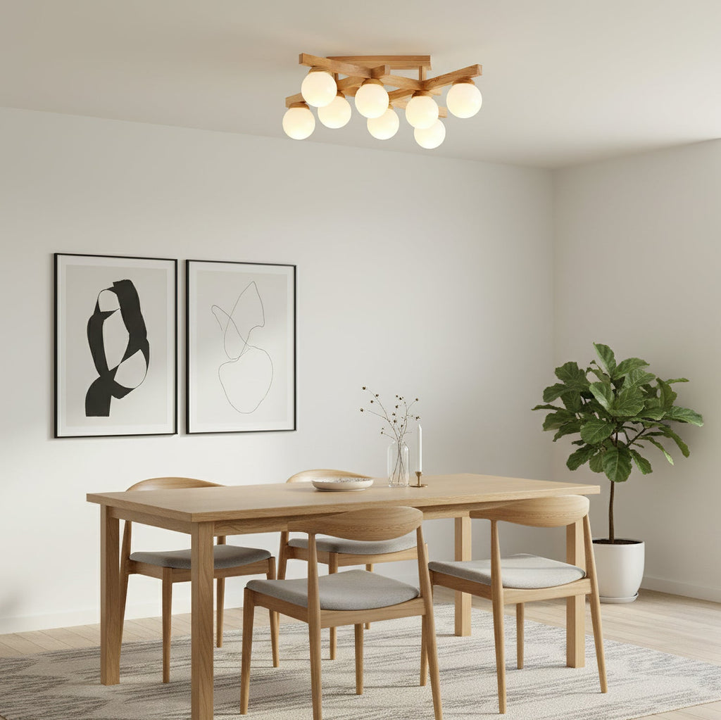Small Clérachic ceiling light with frosted globes above an oak dining table and chairs, with framed line art and a potted plant on the wall side.