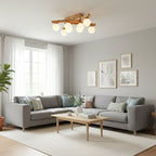 Wood-frame Clérachic ceiling light seen from across a bright living room with a grey corner sofa, a pale rug and tall windows with sheer curtains.