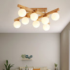 Wood-arm Clérachic ceiling light with eight lit frosted globes, seen from below with a small wall shelf and a plant in the room beneath.