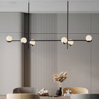 A long Clérachic chandelier with frosted globes on a black bar hangs over a dining area with dried pampas grass.