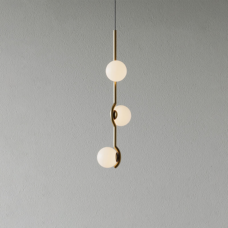 A Clérachic three-globe pendant with a slim gold stem and frosted white globes, on a plain grey wall.