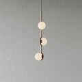 A Clérachic three-globe pendant with a slim gold stem and frosted white globes, on a plain grey wall.