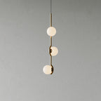 A Clérachic three-globe pendant with a slim gold stem and frosted white globes, on a plain grey wall.