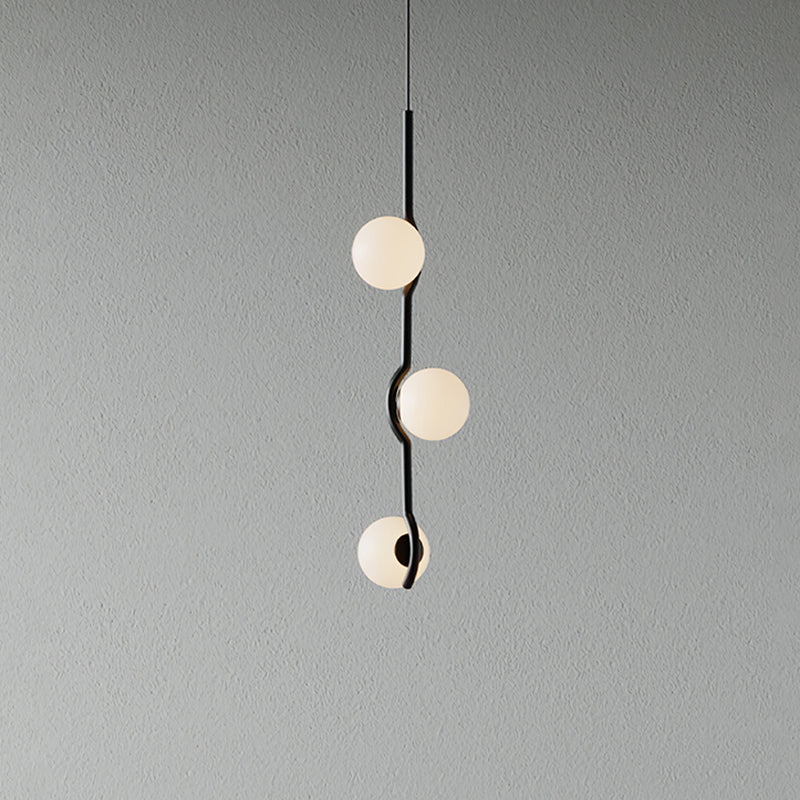 A Clérachic three-globe pendant with a curving black stem and frosted white globes, on a plain grey wall.