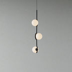 A Clérachic three-globe pendant with a curving black stem and frosted white globes, on a plain grey wall.