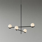 This Clérachic chandelier in black, with four frosted globes on crossing arms, on a plain grey wall.