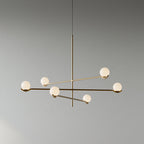 A Clérachic chandelier with six frosted globes, its gold and black arms crossing at different heights, on a plain grey wall.