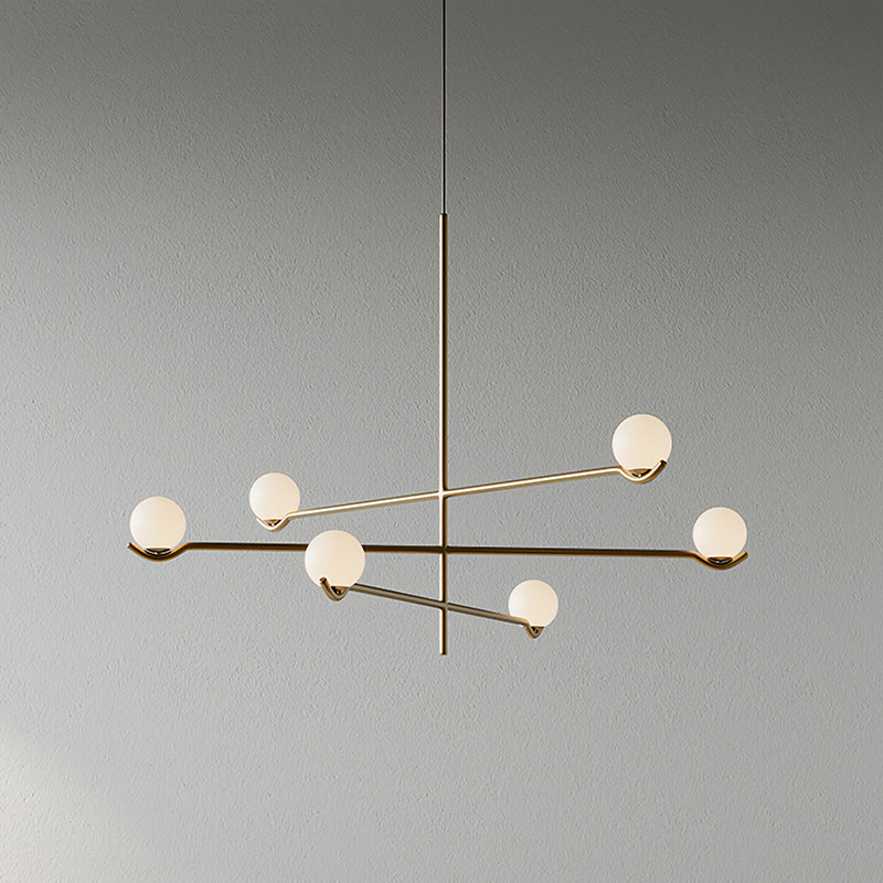A Clérachic chandelier with six frosted globes, its gold and black arms crossing at different heights, on a plain grey wall.