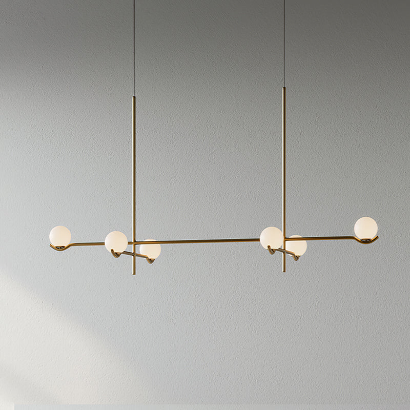 A long Clérachic chandelier in gold on two rods, with six frosted globes along its arms, on a plain grey wall.