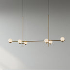 A long Clérachic chandelier in gold on two rods, with six frosted globes along its arms, on a plain grey wall.