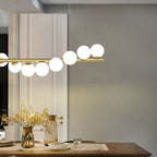 This gold Clérachic Frosted Globe Linear Pendant Light hangs near a mirrored wall above a dining table set with vases of flowers.