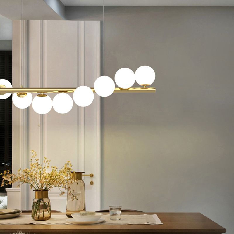 This gold Clérachic Frosted Globe Linear Pendant Light hangs near a mirrored wall above a dining table set with vases of flowers.