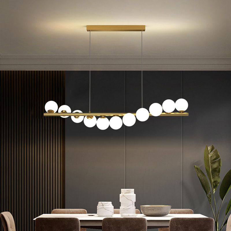 A gold Clérachic Frosted Globe Linear Pendant Light spans a dining room ceiling framed by wood slat paneling and crown molding.