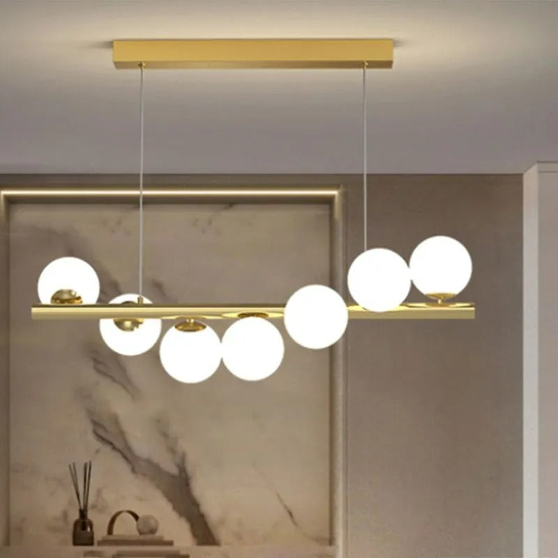 The gold Clérachic Frosted Globe Linear Pendant Light hangs against a marble backsplash styled with a reed diffuser and books.