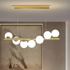 The gold Clérachic Frosted Globe Linear Pendant Light hangs against a marble backsplash styled with a reed diffuser and books.