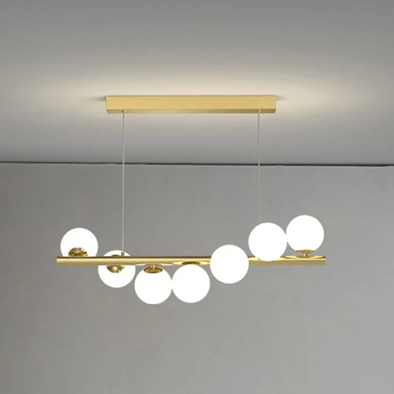 A close view of the gold Clérachic Frosted Globe Linear Pendant Light suspended from its canopy against a plain grey wall.