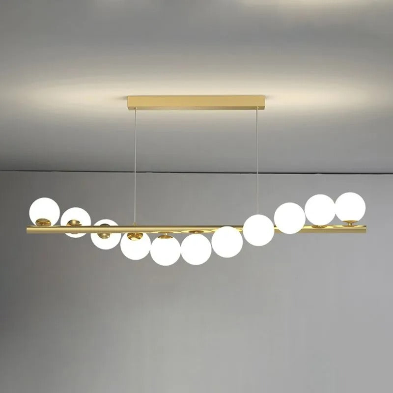 This gold Clérachic Frosted Globe Linear Pendant Light shows its full run of frosted globes staggered along the bar.