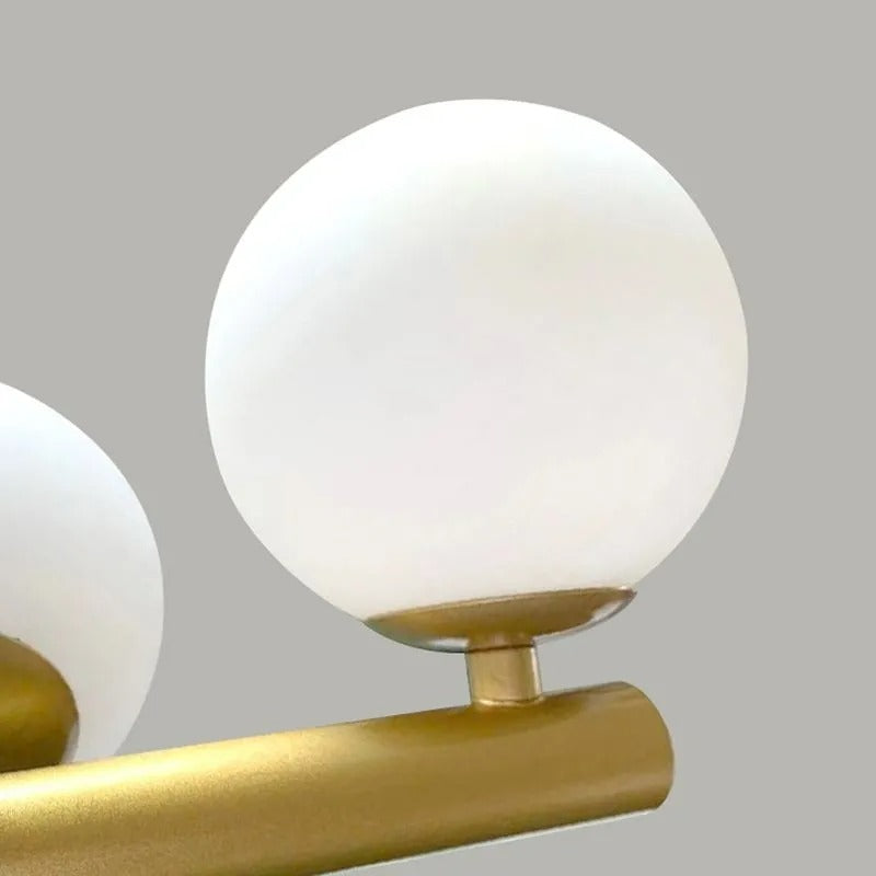 A macro view of one frosted glass globe on the Clérachic Frosted Globe Linear Pendant Light, seated on its gold bar.