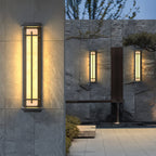Close view of a lit Clérachic wall light on a grey slate wall, with two smaller lights glowing on the stone wall behind.