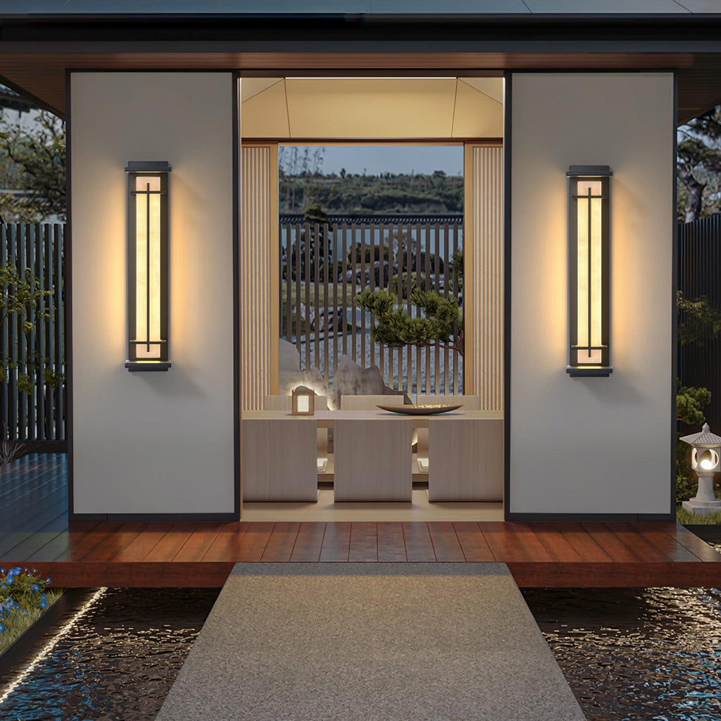 A pair of lit Clérachic wall lights flanking an open pavilion entrance, with a timber deck and stone path leading in.