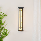 This Clérachic wall light on a cream wall, switched off, with its dark frame and a green plant to one side.