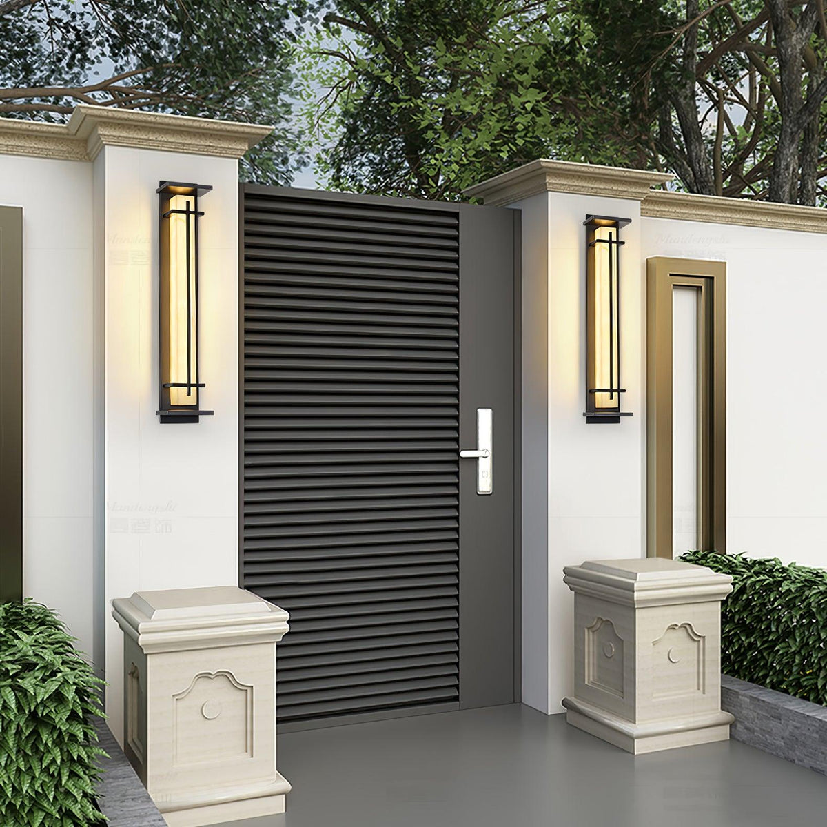 Two Clérachic wall lights lit on white gate piers, either side of a dark louvred gate with stone planters at the foot.