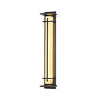 Straight-on view of a lit Clérachic wall light with a warm glowing shade between two dark metal bars, on white.