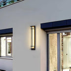 A single lit Clérachic wall light on a pale rendered wall beside a window and a sliding glass door.
