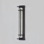 Unlit tall wall light with a marbled pale shade behind slim dark bars, shown on a pale grey wall; a Clérachic design.