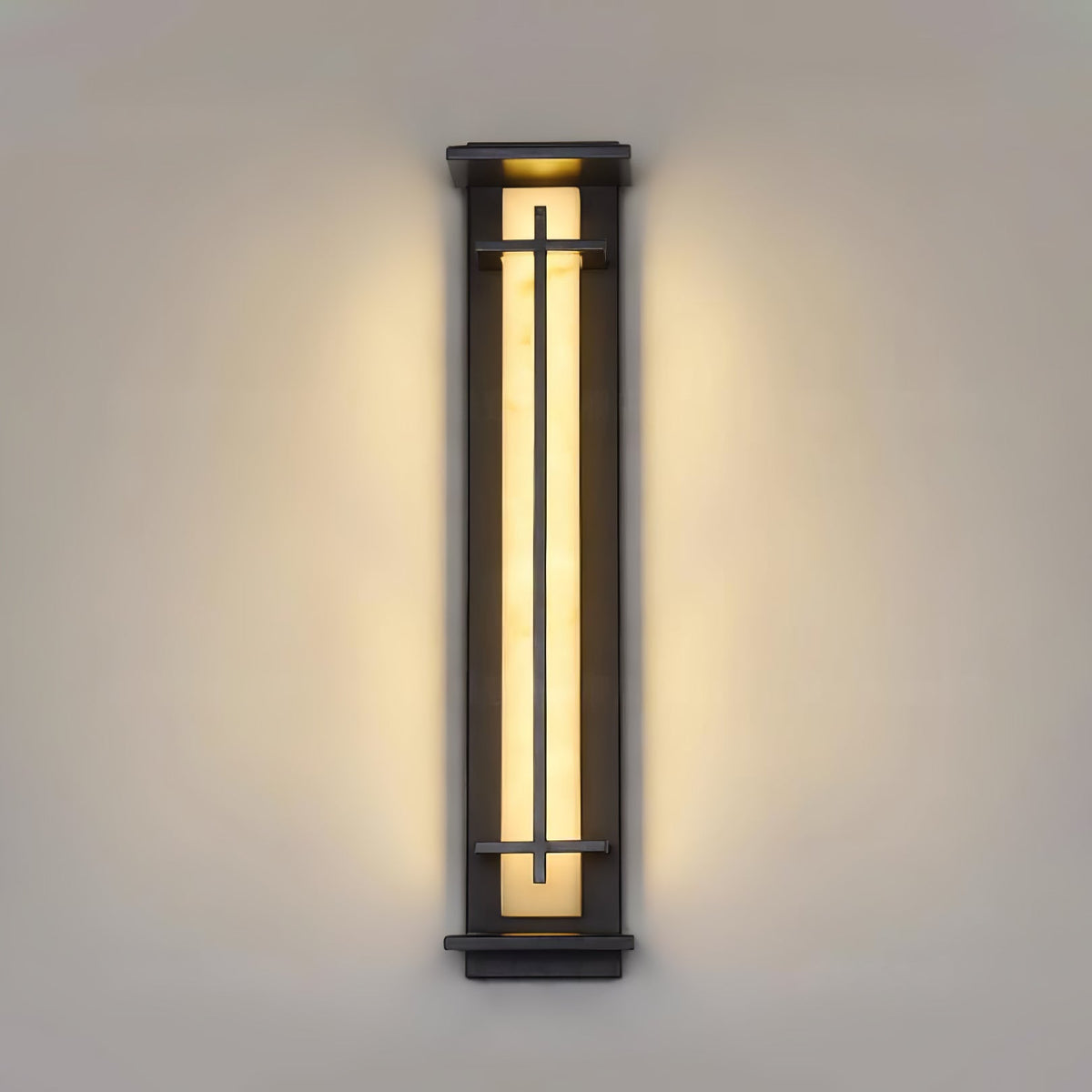 Long, slim Clérachic wall light lit warm on a stone-coloured wall, the light spreading evenly either side of the frame.