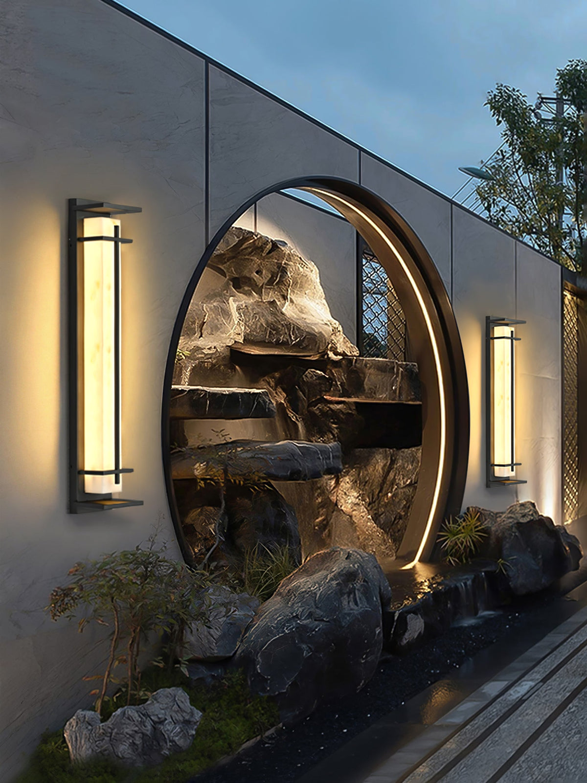 Narrow view of two Clérachic wall lights on either side of a round garden opening with a lit rock feature behind.