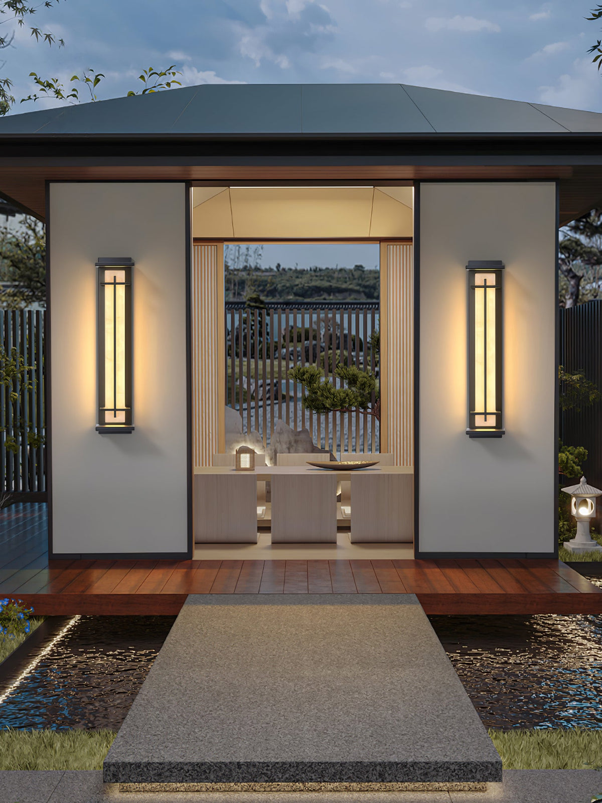 Two lit Clérachic wall lights either side of a pavilion doorway, with a timber deck and a stone path across water.