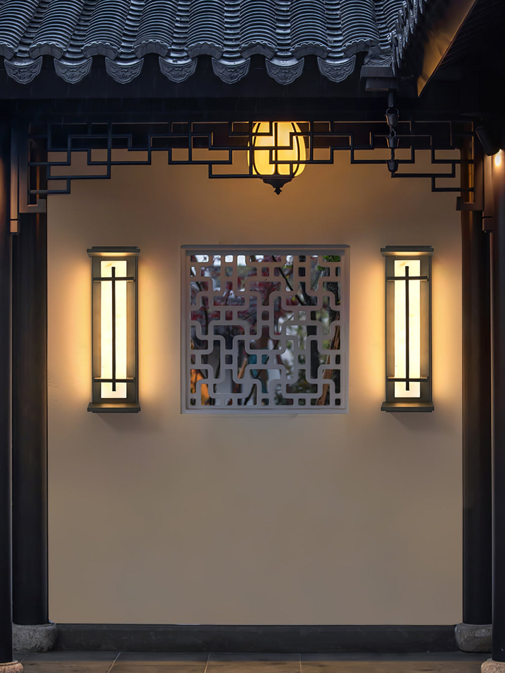 A pair of lit Clérachic wall lights framing a lattice window panel on a cream wall, under a tiled eave with a hanging lantern.