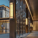 Clérachic wall lights lit along a dark colonnade with a decorative screen, with a building glimpsed in the dusk beyond.