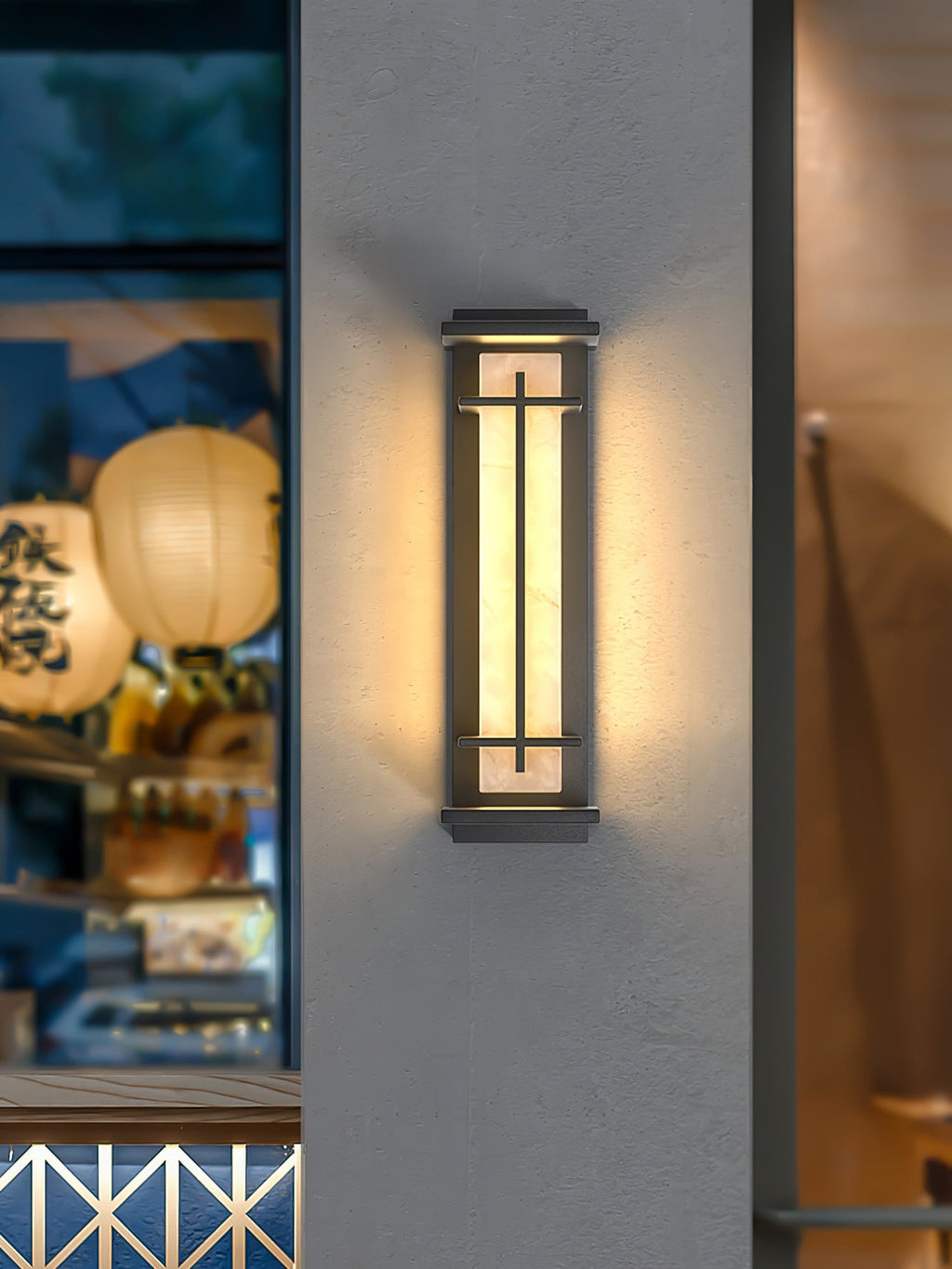 A single lit Clérachic wall light on a pale wall, with paper lanterns and a shopfront glimpsed behind a dark edge.