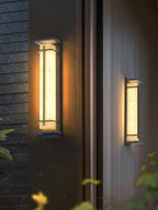 Two lit wall lights at different heights on dark panelled walls, the closer one in sharp focus; from Clérachic.